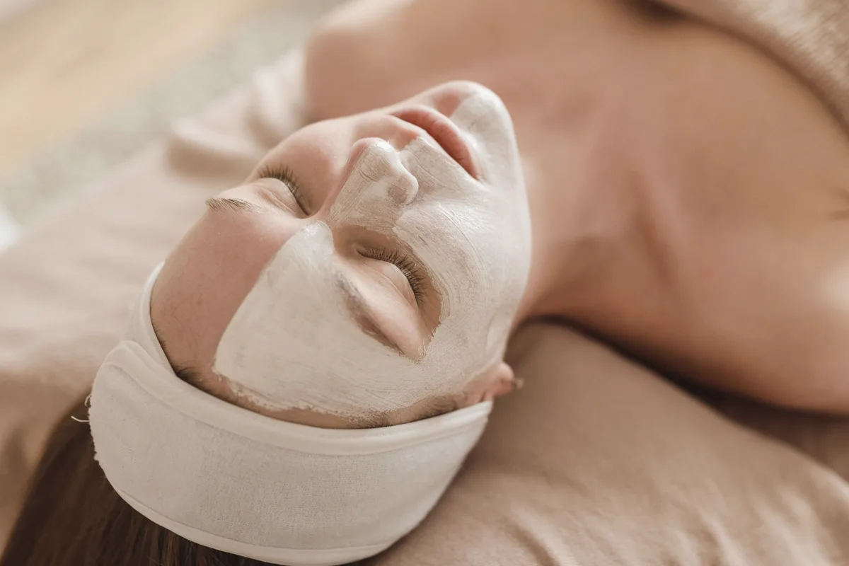 A client lying back with eyes closed, wearing a white face mask and a cloth headband