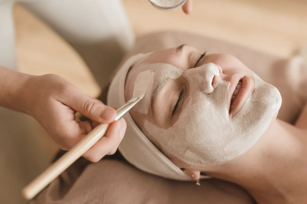 An esthetician brushing a white mask onto a smiling client's face