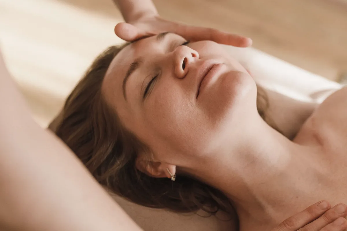 A client with eyes closed as an esthetician's hands rest on her forehead during a facial massage